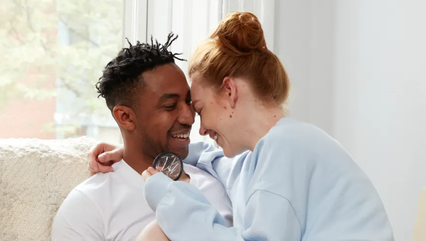 Smiling couple sitting closely as one person holds a menstrual disc in hand