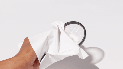Hand holding a menstrual disc partially wrapped in eco disposal pouches against a white background