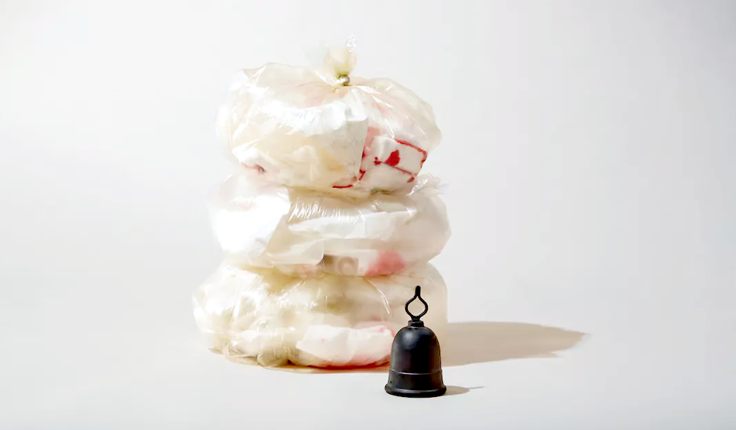 Menstrual cup placed beside stacked bags of used disposable period products