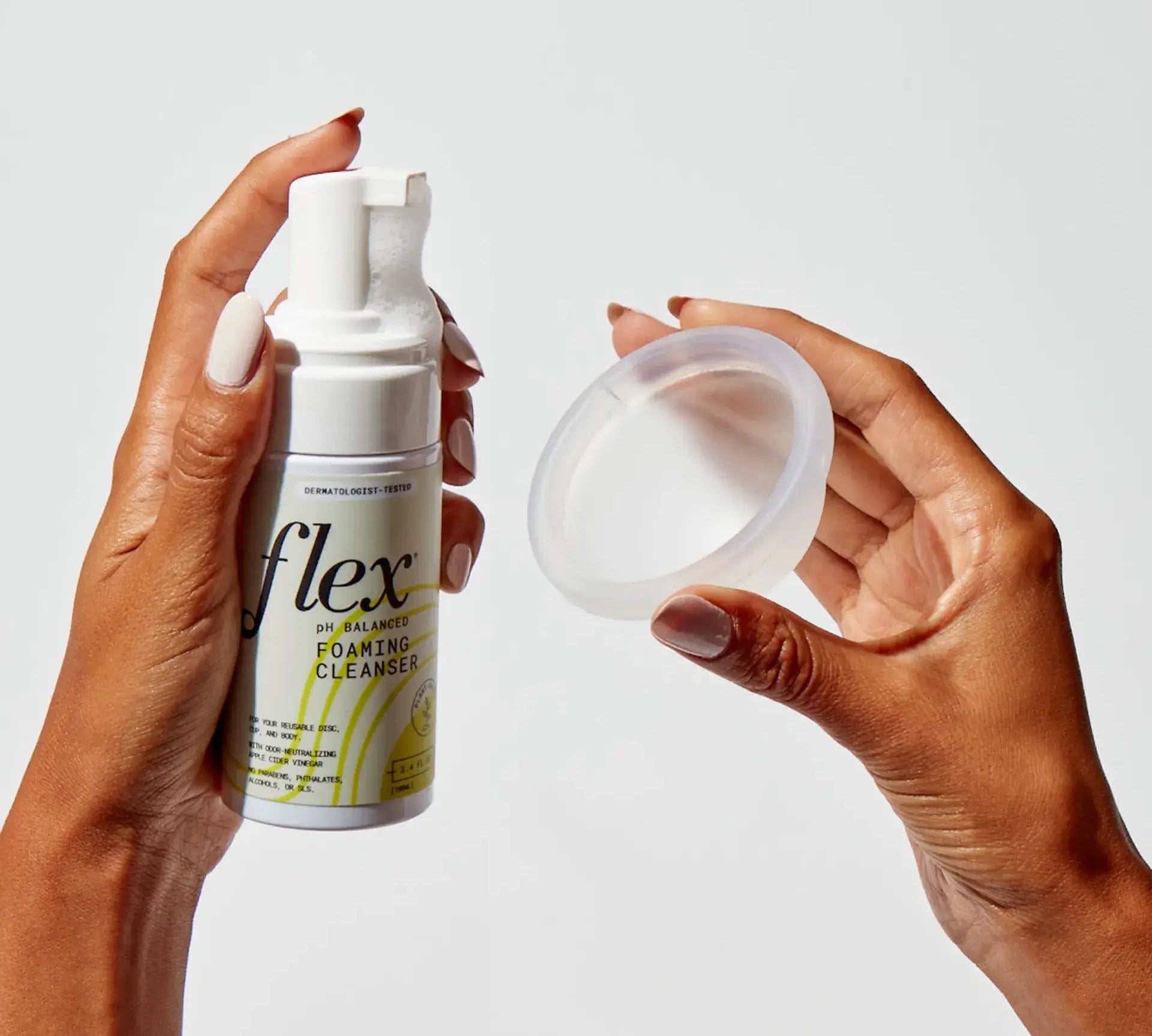 Hands holding a menstrual disc and a bottle of foaming cleanser