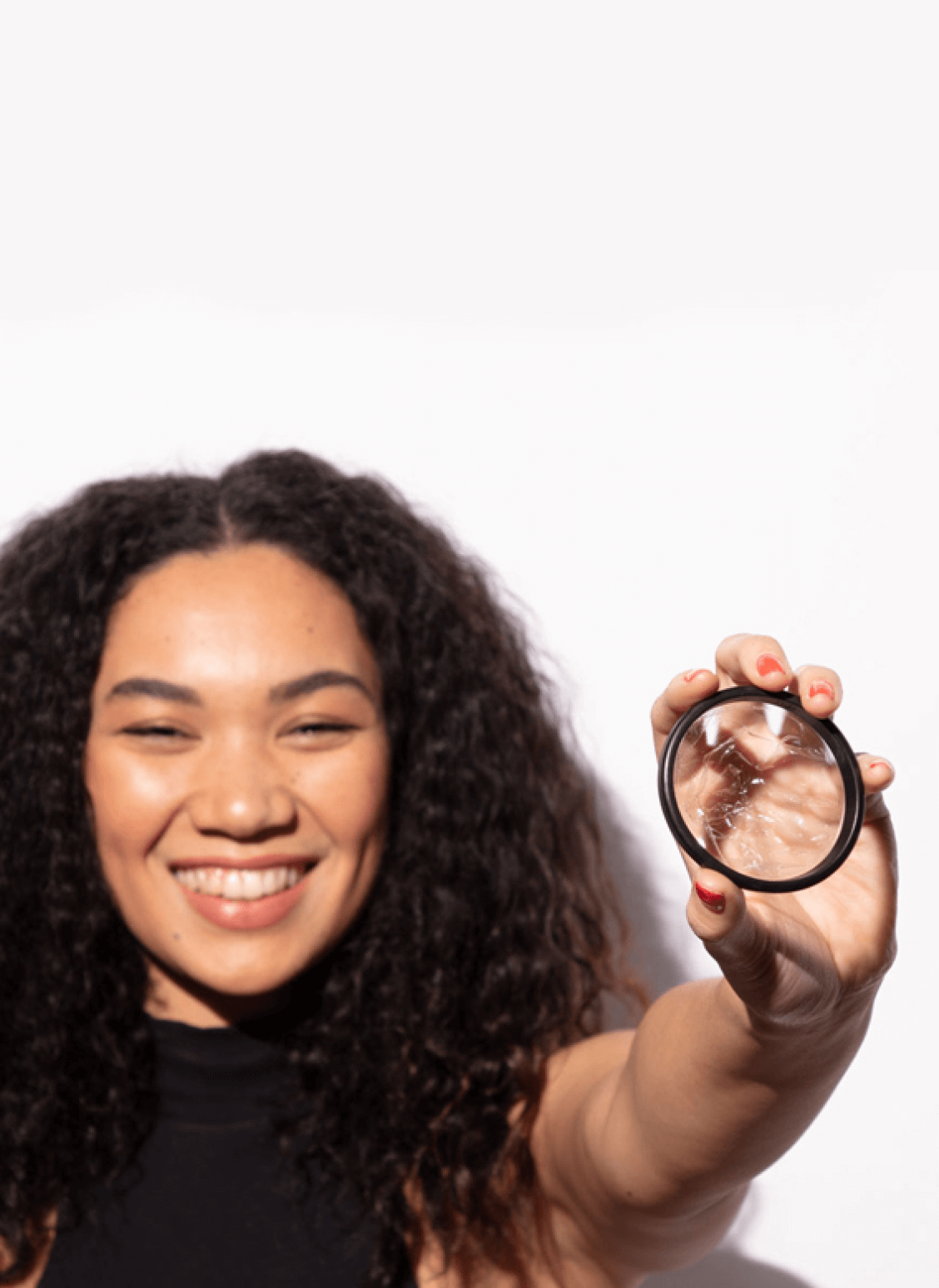 Smiling person holding a menstrual disc in one hand against a plain background