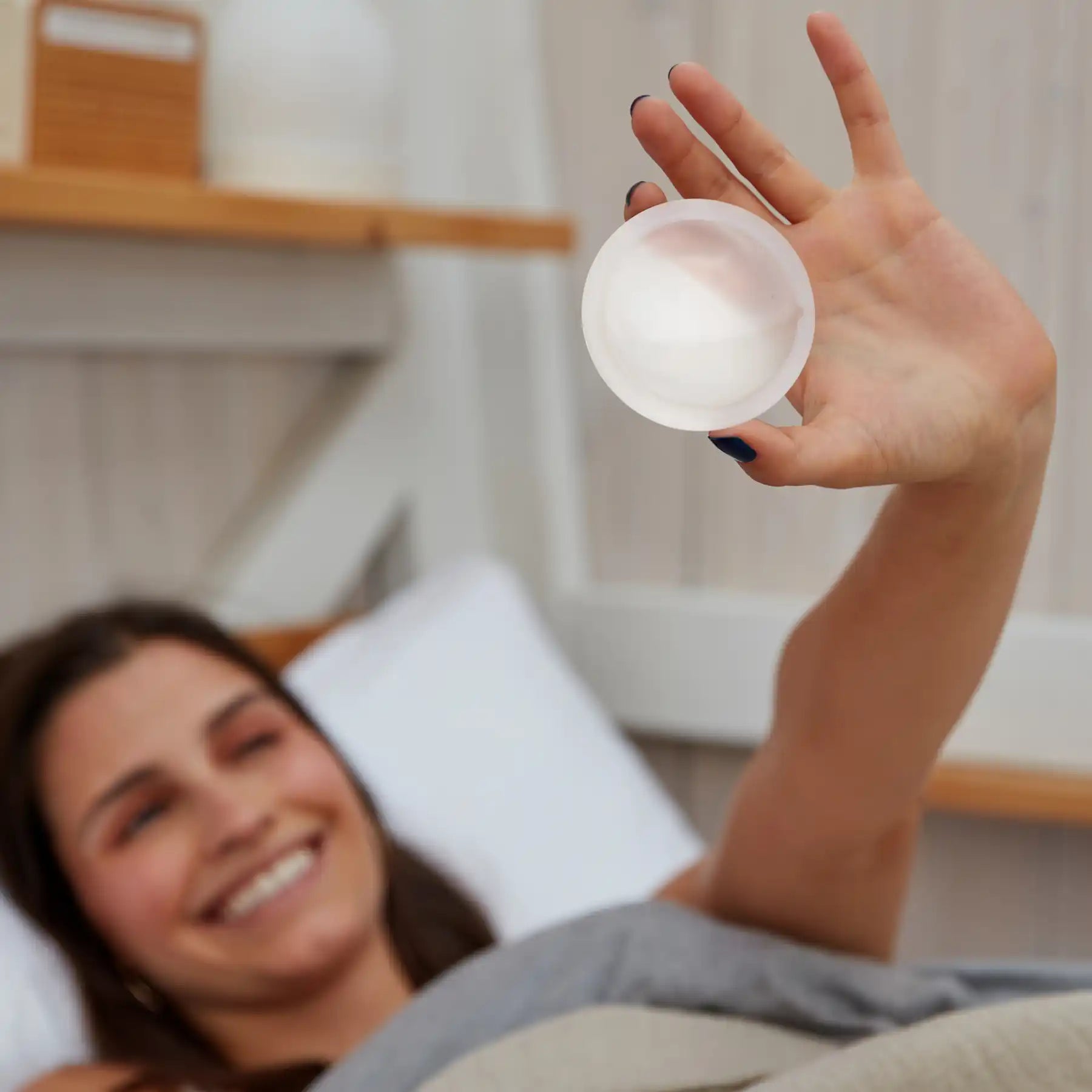 Person lying in bed holding up a reusable menstrual disc
