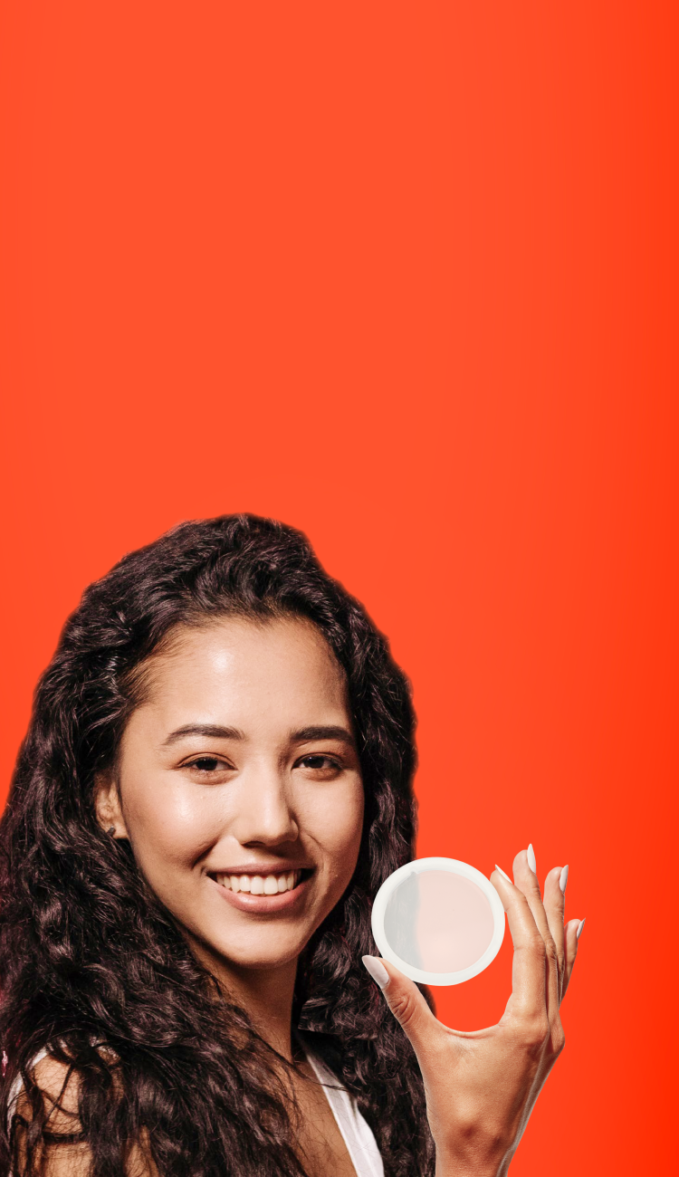 Smiling woman holding a reusable menstrual disc in front of a bright background